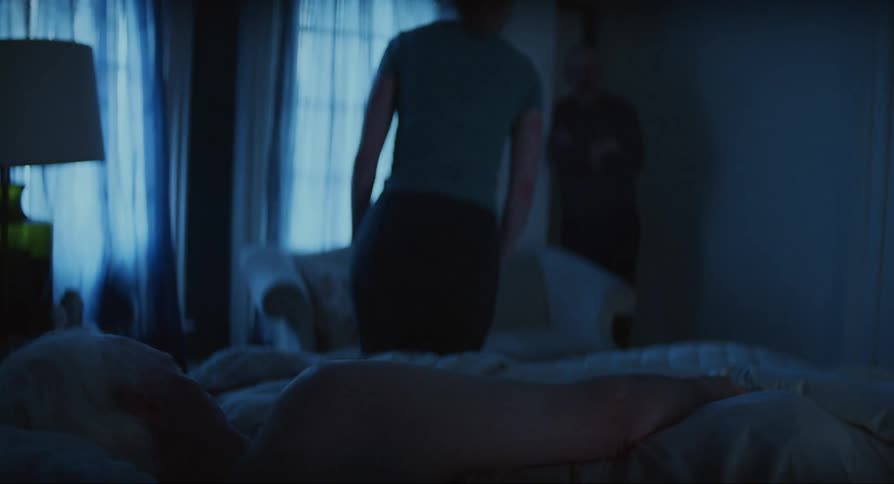 Woman taking care of an elderly woman stands up from bed and leaves the bedroom