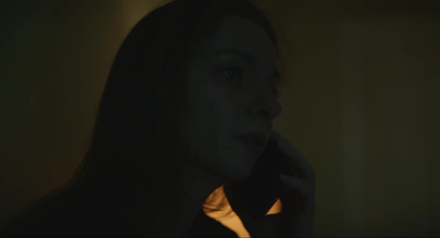 A sad woman is talking on her cell phone in a dark room