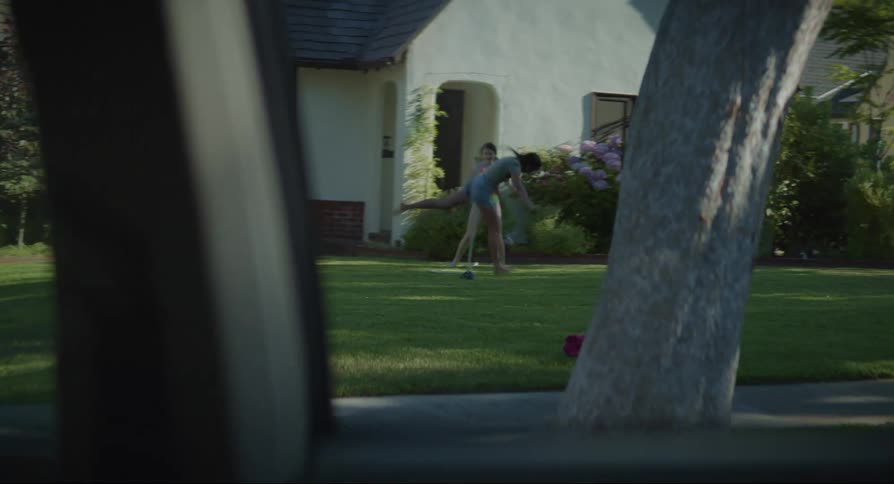 Mother and teenage daughters playing in the front yard seen from a moving car