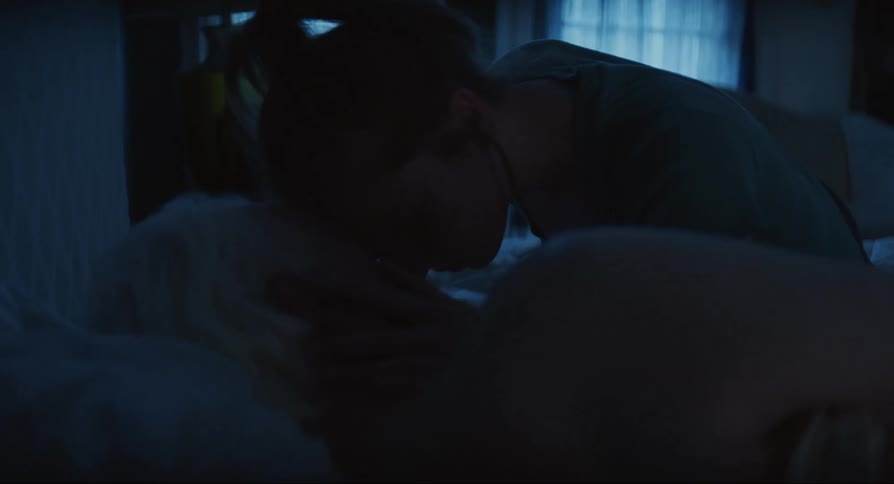 A young woman caresses her father who is an elderly man who is lying asleep in a bed