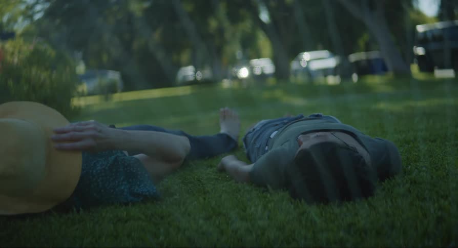 Girl with ponytail and swimsuit jumps over girl and woman lying on green lawn in the park