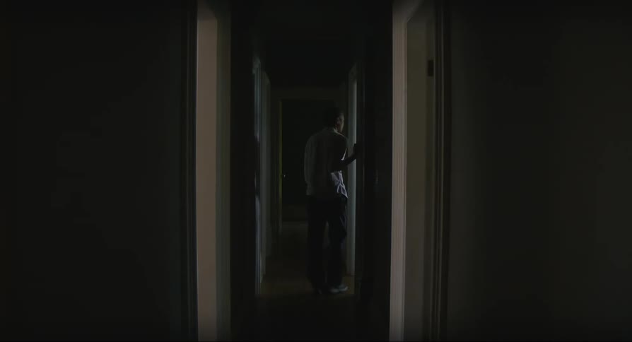 Man walking down the hallway of a house stopping beside a door with his back turned