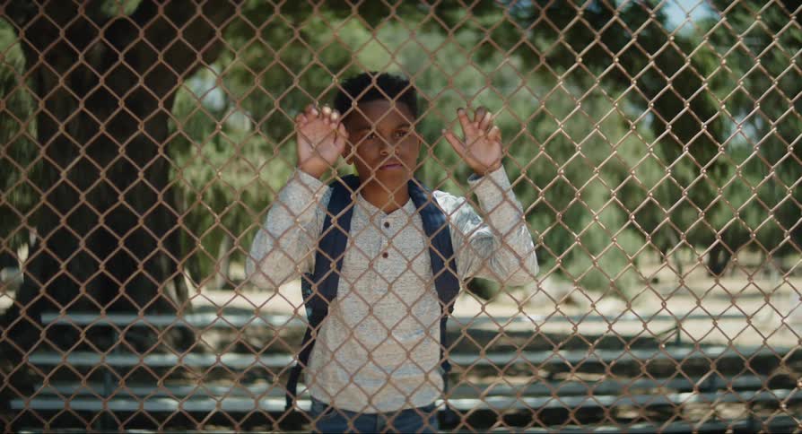 Boy with a sad facial expression placing his hands on a railing and observing