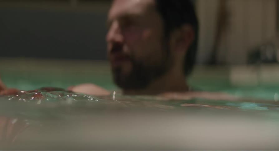 Mother in the pool holding her baby son while the father plays with water beside them