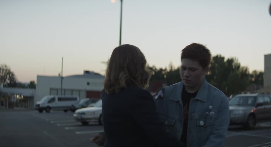 An upset mother hugs her son in a store parking lot at dusk
