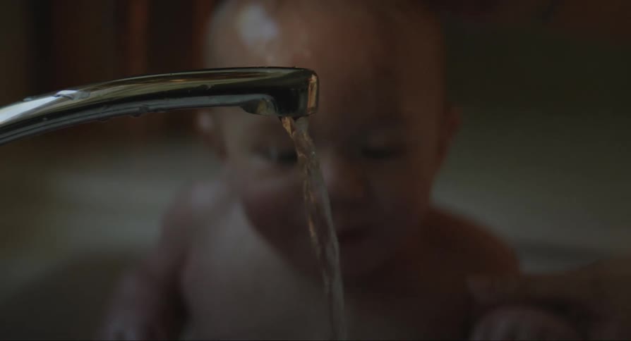 A person bathing a baby in a sink faucet