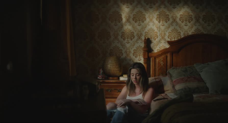 A young woman sitting by a bed sighing and checking her phone