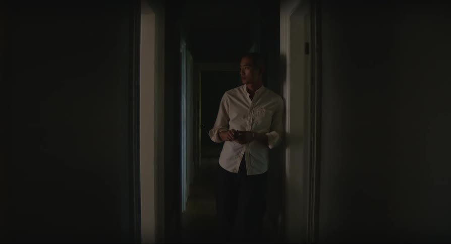 A man walks down a hallway and leans against a wall and is thoughtful
