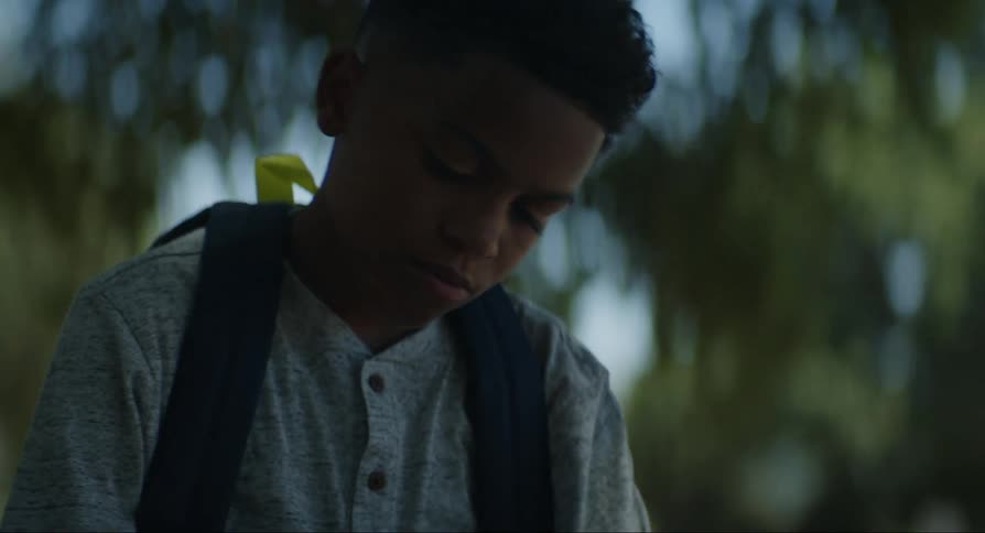 A boy is sitting and writing on a bench with a stick