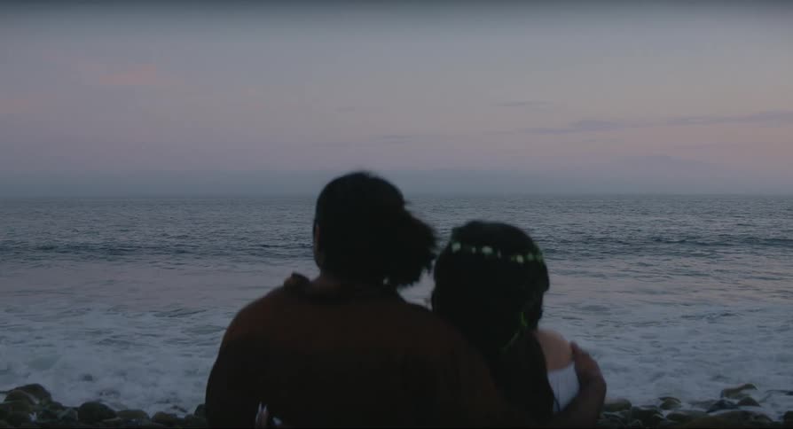 A man and a woman are sitting together along the coast as waves roll into shore
