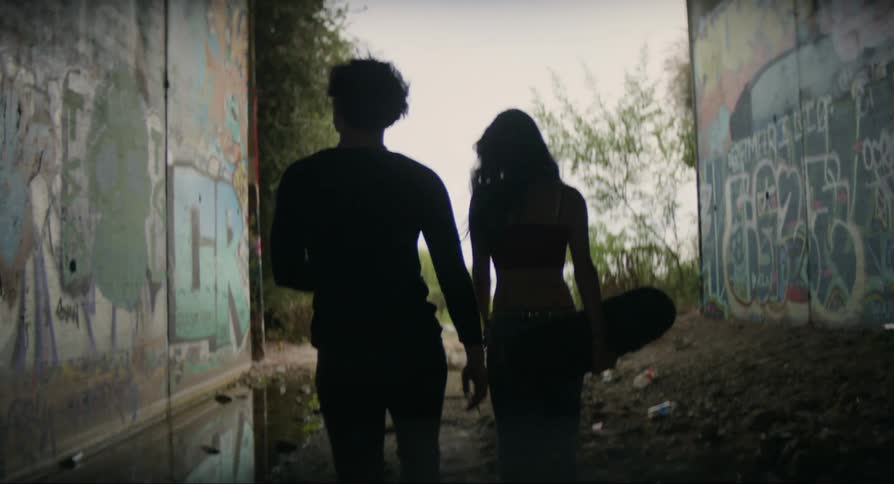 A man and a woman with a skateboard in their arms are walking through dirt and puddles of water
