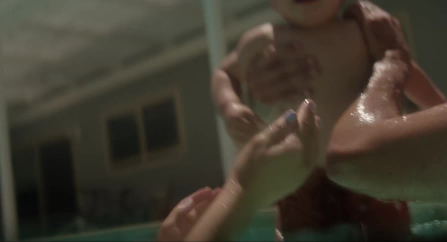 Young father and mother playing and kissing their baby son on a swimming pool outdoors during day time