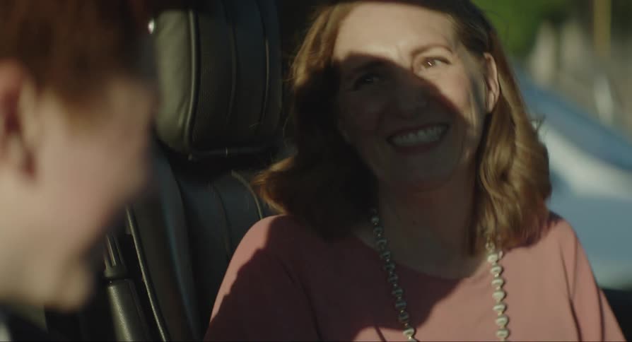 A woman in a car smiles and laughs at what the boy sitting next to her is doing then gives him a hug