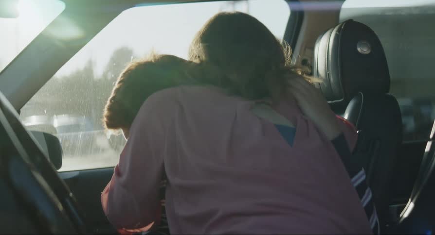 Mother congratulates son with a hug as he reads letter while they sit in parked vehicle