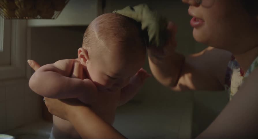 Mother holding her infant song after bathing him at the kitchen sink as the sun shines through the window