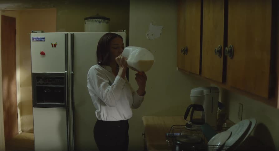 Woman with white shirt and black pants uses a smartphone and drinks milk from a gallon in the kitchen