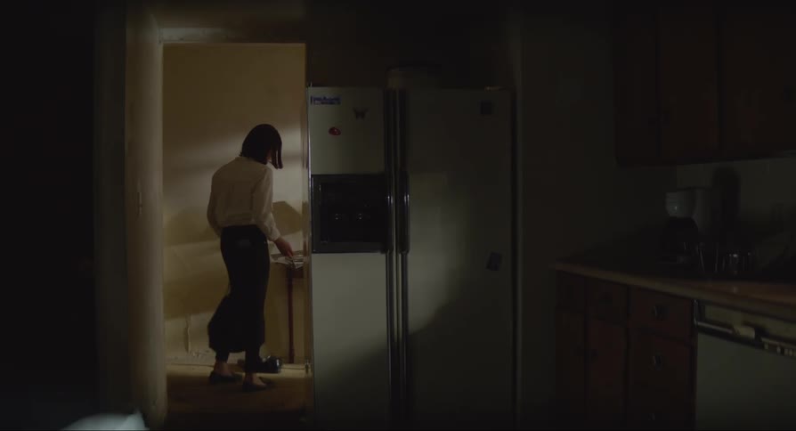 Woman wearing white shirt and black pants enter house turns on the lights and open the fridge in the kitchen