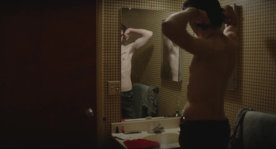 Man inside the bathroom looking at himself in the mirror and striking poses with his arms