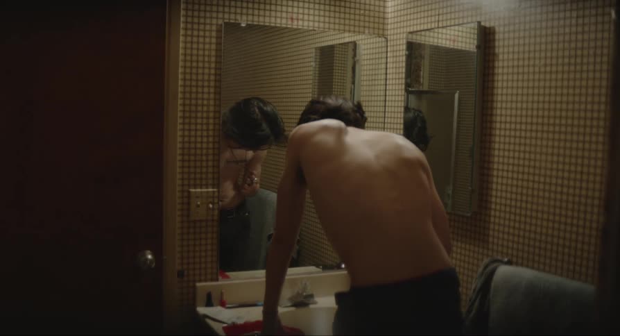 Shirtless man facing the mirror and kissing his necklace