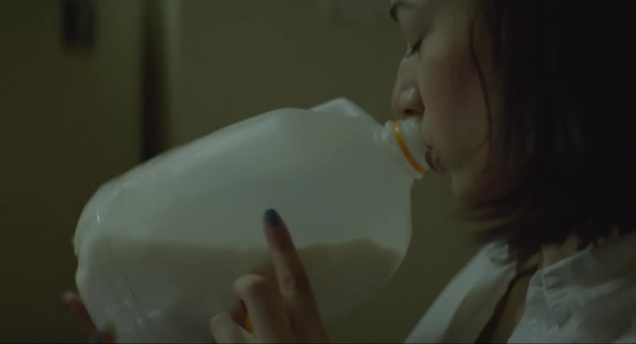 Close up of a woman grabbing a milk carton out of the fridge and drinking from it