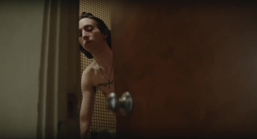 A man in a small room brushes his hair with his hand and then shuts the door
