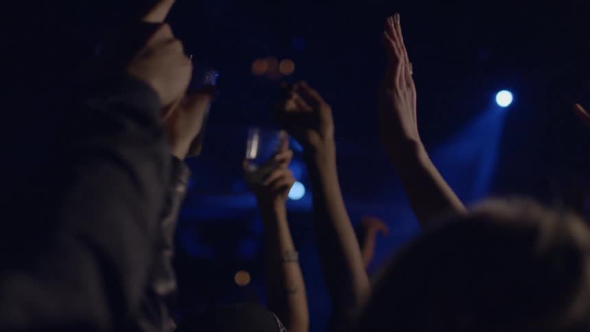 People raising their hands and drinks in the air while jumping around in a club