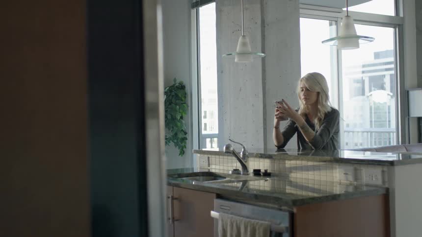 Woman using her smartphone while sitting at the counter in her kitchen