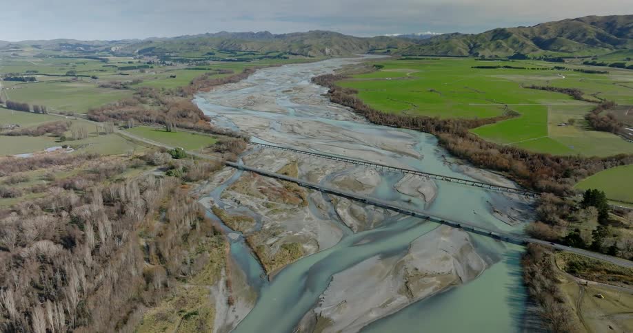 Drone view of a river flowing through a flat land with roadways and bridges traveling over the river