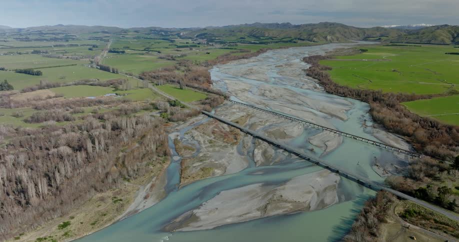 Aerial view of agricultural fields with a large lake between them featuring bridges and vehicles passing by
