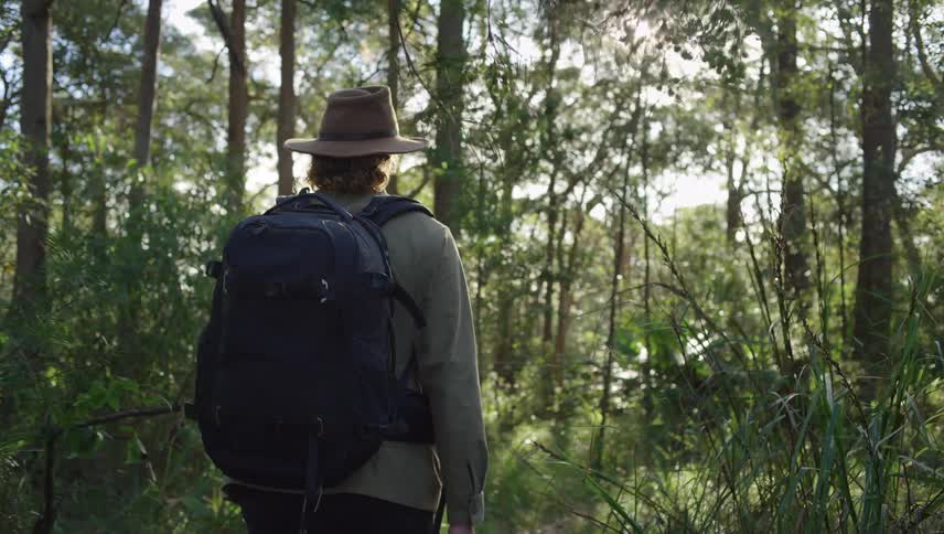 Man carrying a backpack and camera walks through the forest
