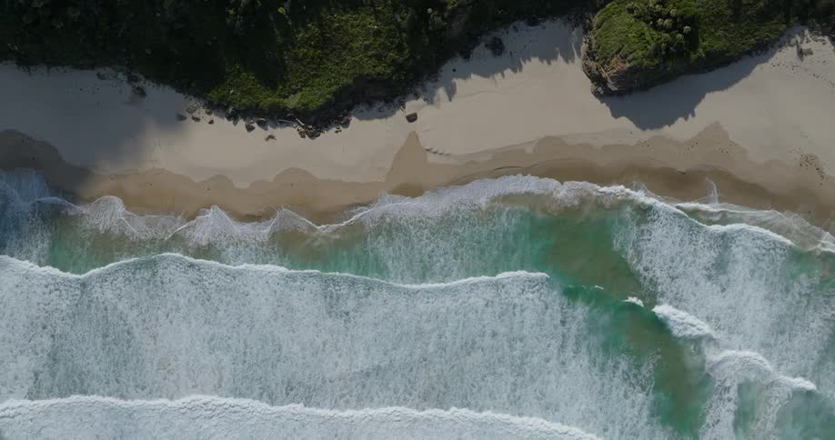 Aerial view of ocean waves breaking against the white sand beach