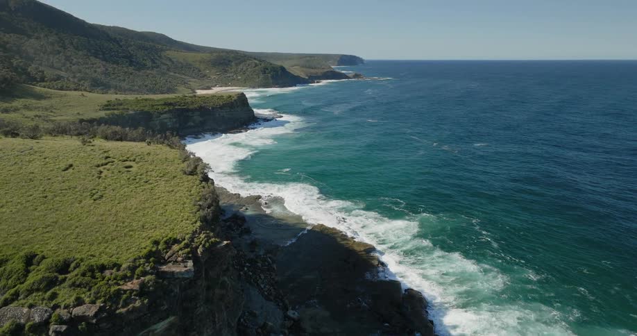 Waves roll into shore as trees and plants grow on the mountain along the coast