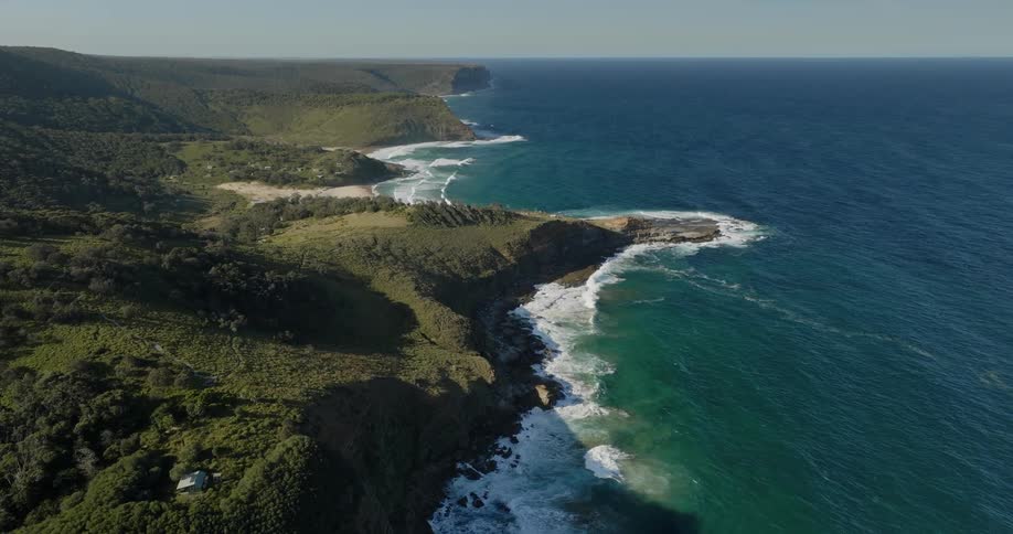 An aerial shot of grassy cliffs and a beach near the ocean in the day