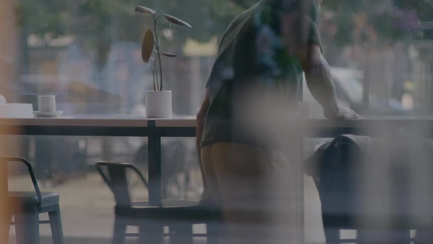 A man pulling out a chair in front of a cafe bar counter in front of a large window looking at the city
