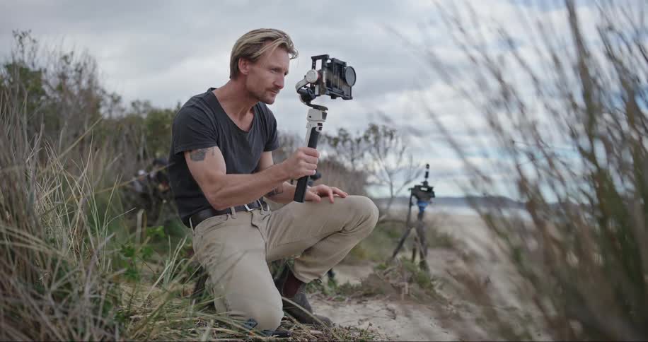 Man crouched down holding a professional camera in an outdoor environment on the beach