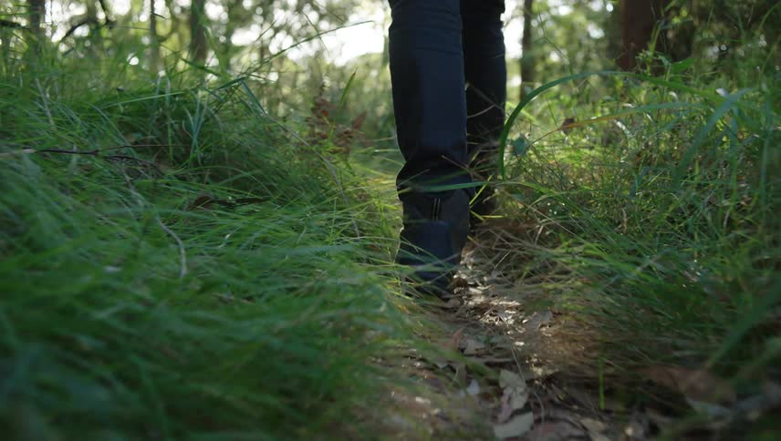 Man wearing dark jeans and boots walks along dirt track in the woods