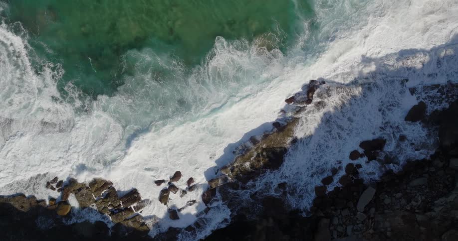 Clear water waves splash against rocks along the coast as they roll into shore