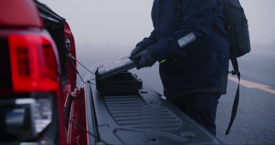 Man wearing cold weather gear unpacks equipment from truck on a foggy winter day