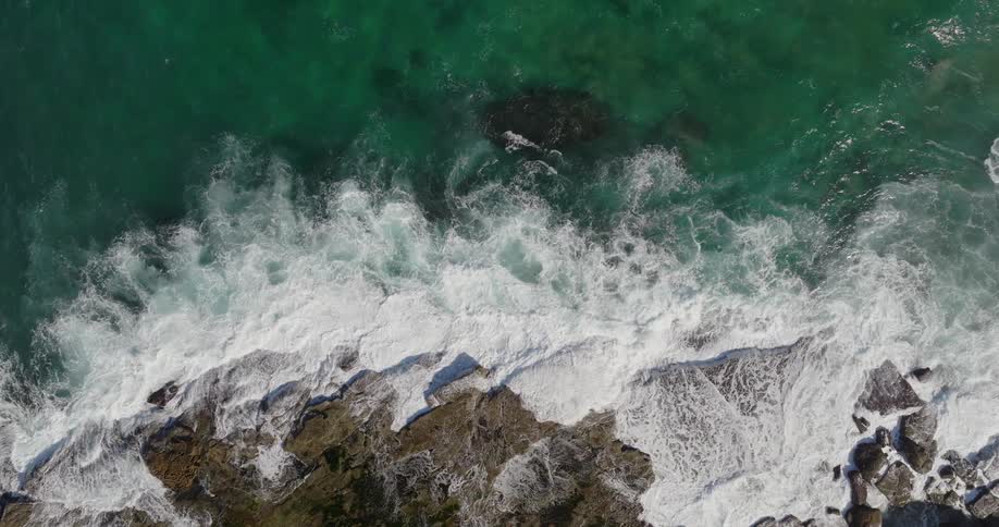 Aerial view of a crystalline sea with waves crashing against rocks