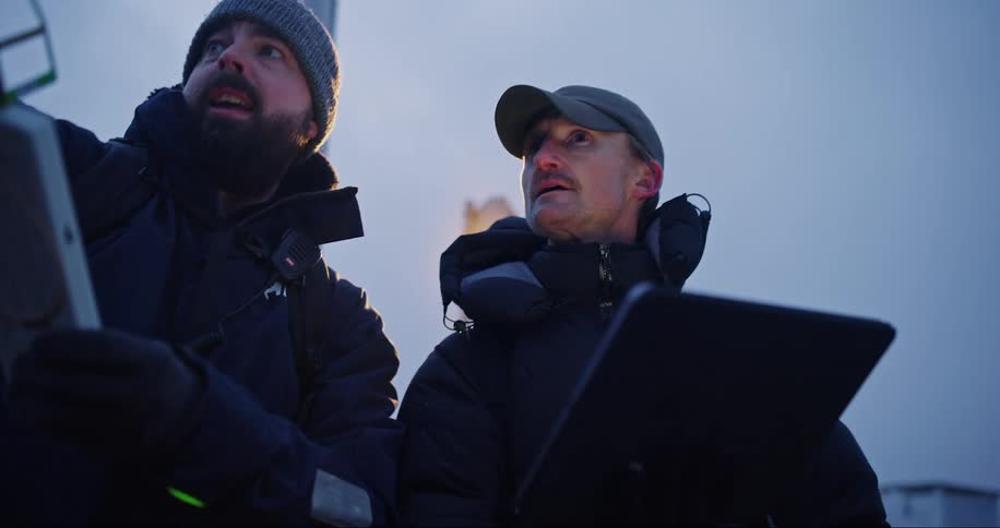Two men talking one of them holding a tablet and the other holding a device with an antenna