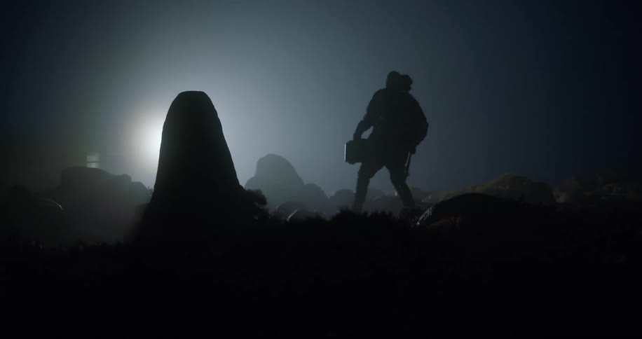 A man walking in a night environment towards a flare of light