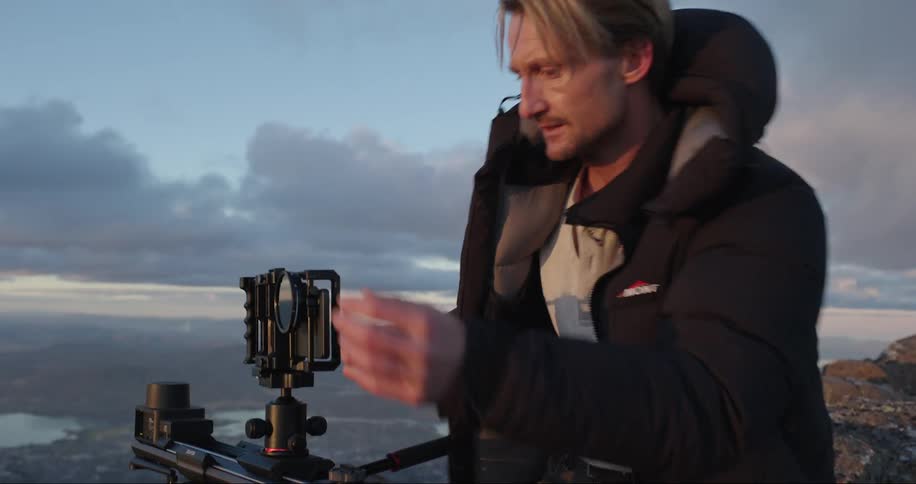 Man wearing a thick jacket takes measurements with equipment on a mountain top