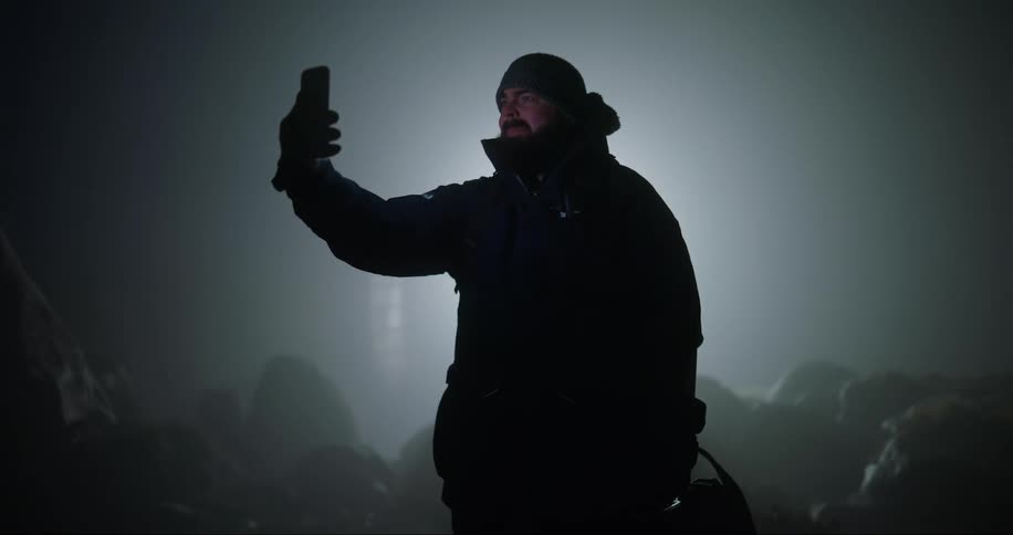 Man using a cellphone holding it up to his face and talking to someone with a smile in a natural outdoor setting at night