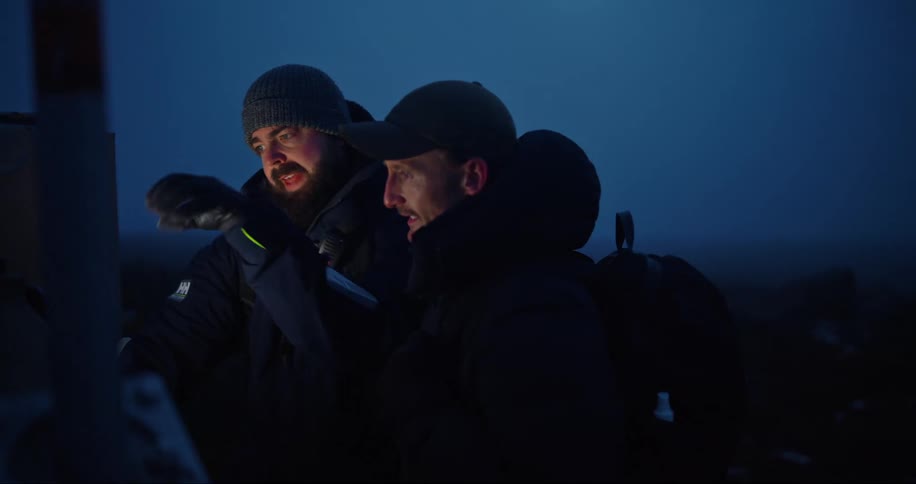 Two men wearing hats and coats standing outside having a conversation at night