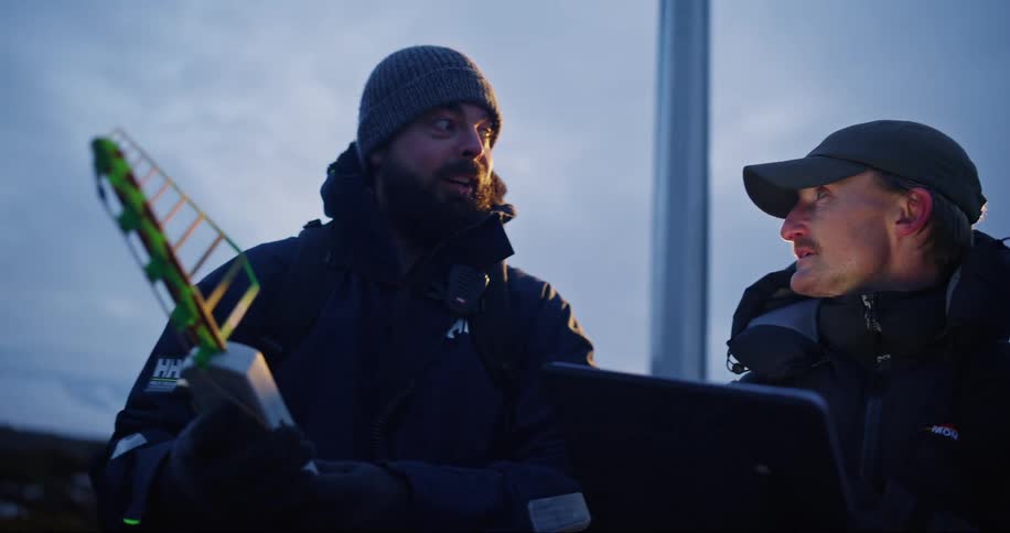 Two coworkers consult computer while working outdoors in cold weather