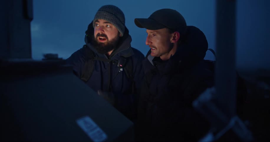 Two men in warm clothing are talking and arranging an object