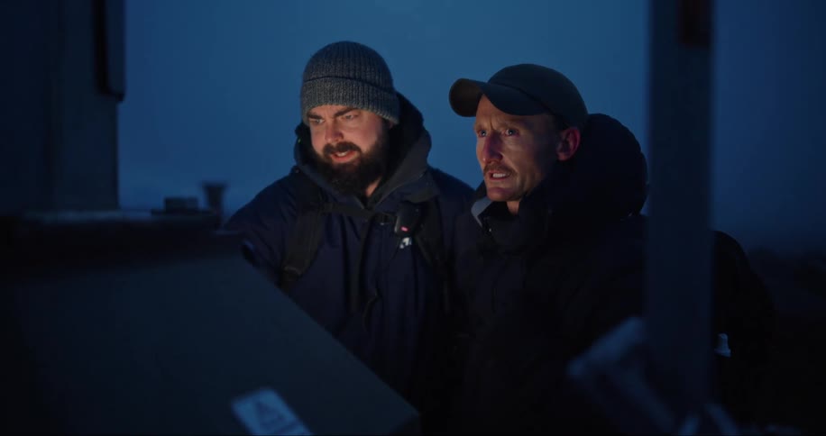 Two men in warm clothing are working on a machine