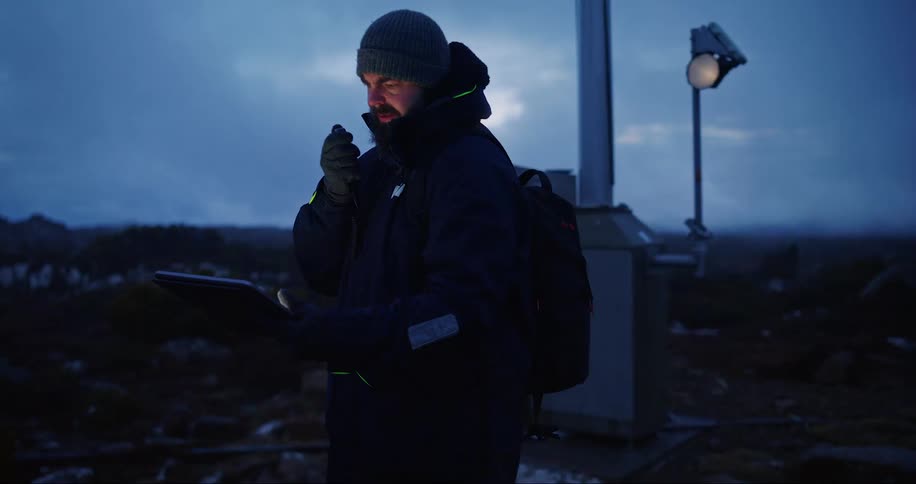 A man is talking on a communicator and holding a tablet during the sunrise