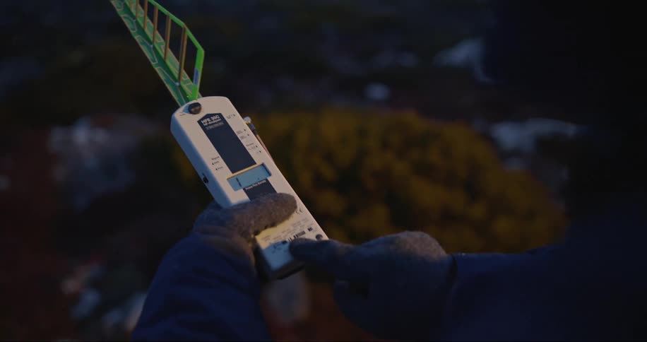 Closeup of gloved hands manipulating a radiation EMF meter