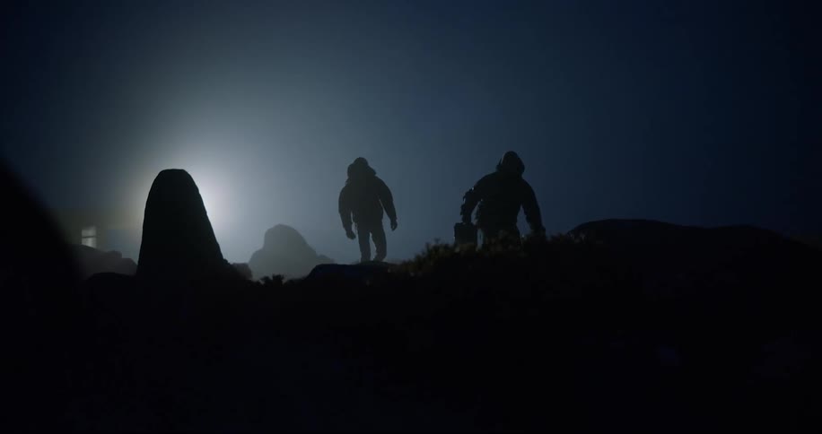 Two people walking at night in an outdoor setting with one of them carrying a briefcase
